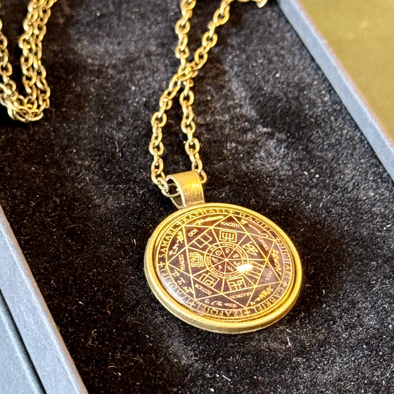 A gold-colored pendant necklace with a circular medallion featuring an intricate design.