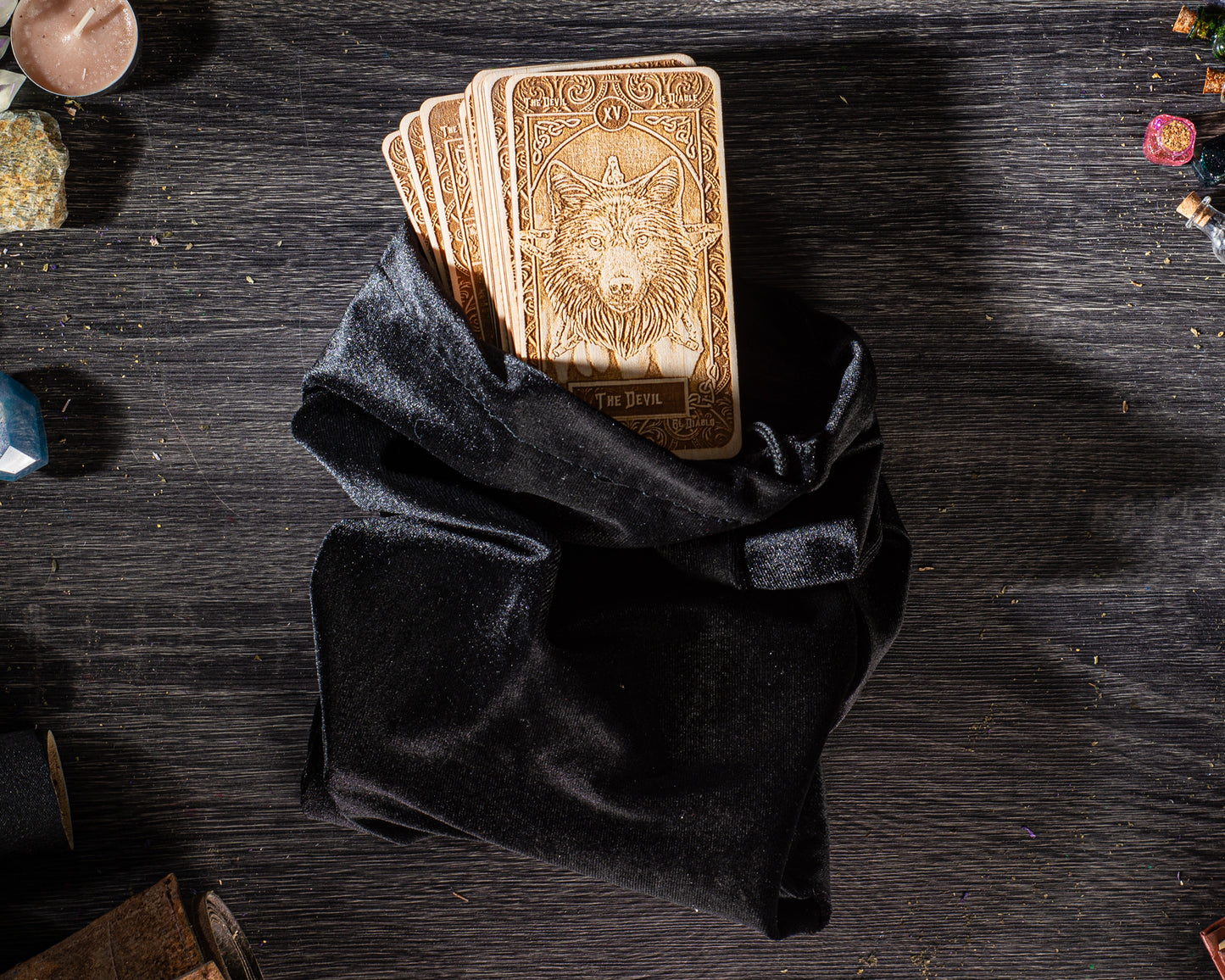 A black velvet pouch containing several wooden tarot cards is placed on a wooden surface.