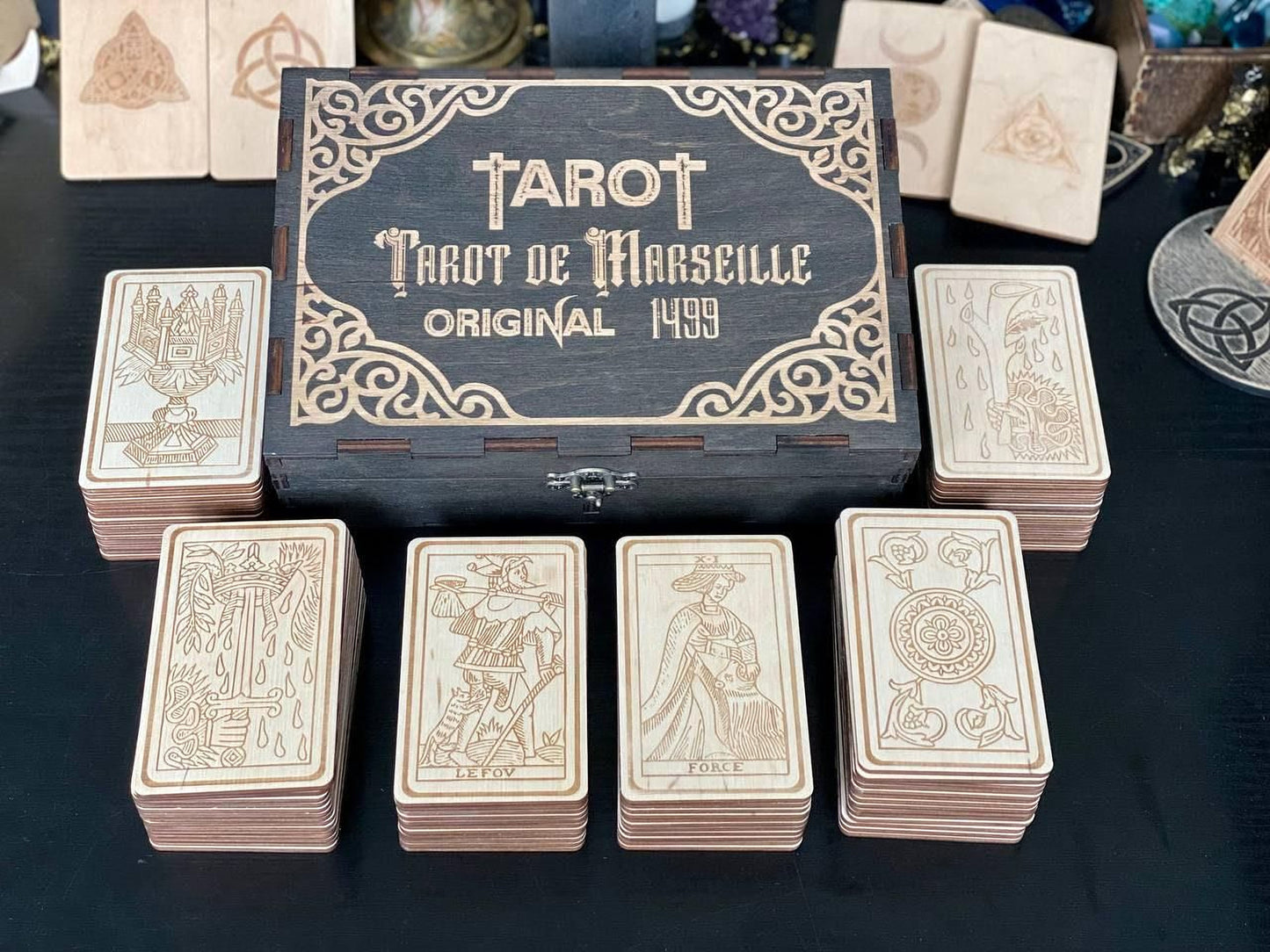 a collection of tarot cards and a wooden box with the text "Tarot de Marseille" on it. The cards are arranged in stacks on a table, and the box is placed in the center of the image.