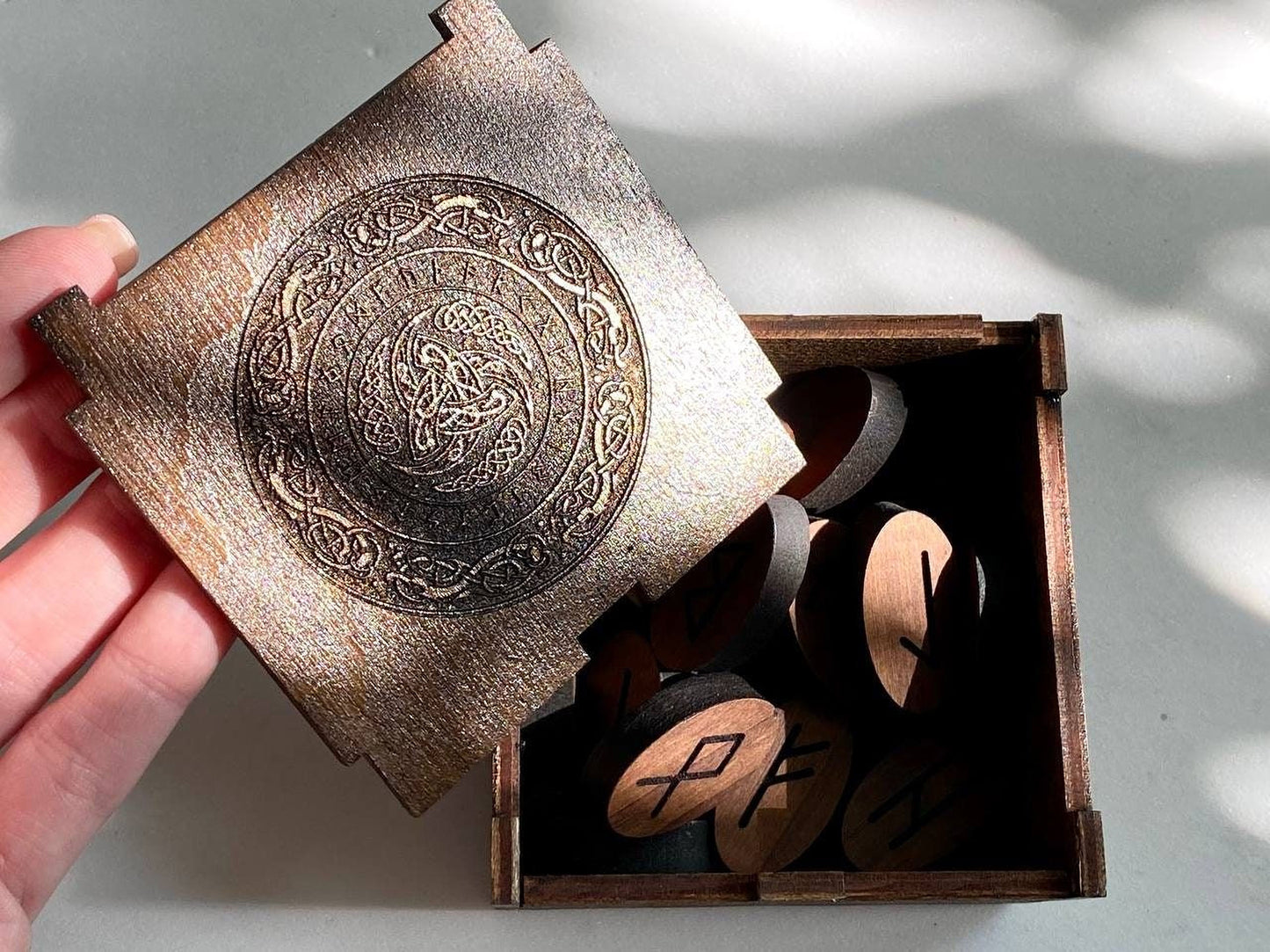 A wooden box with a lid, containing several wooden pieces with carved symbols on them.