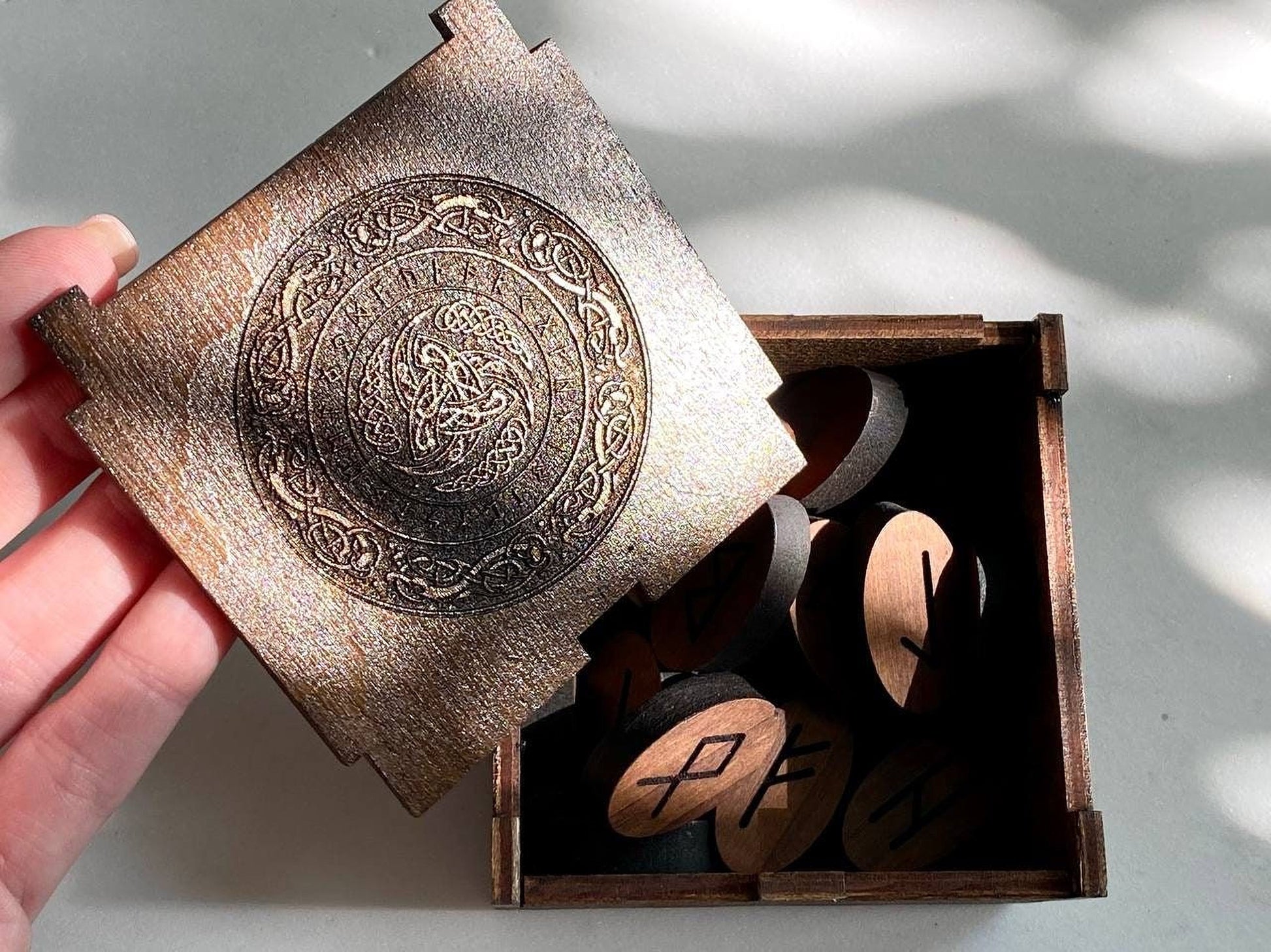 A wooden box with a lid, containing several wooden pieces with carved symbols on them.