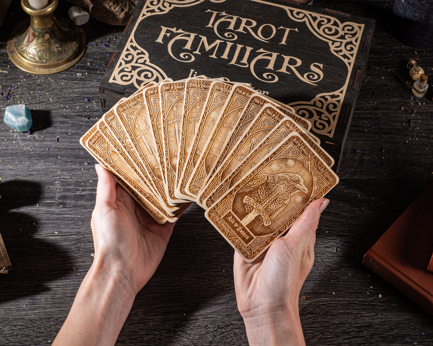 A person's hands holding a deck of tarot cards, with a book labeled "Tarot Familiars" visible in the background.