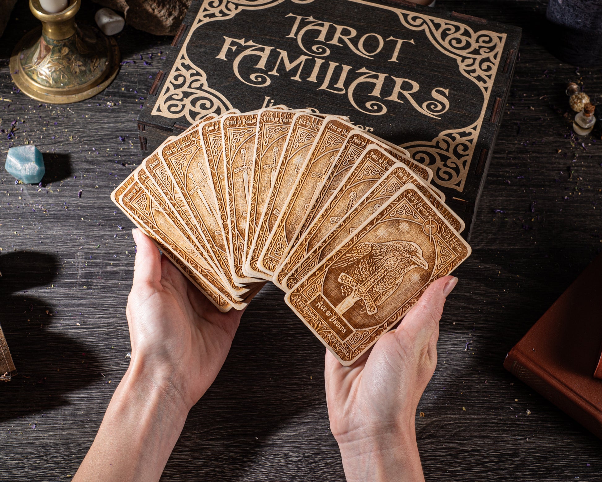 A person's hands holding a deck of tarot cards, with a book labeled "Tarot Familiars" visible in the background.