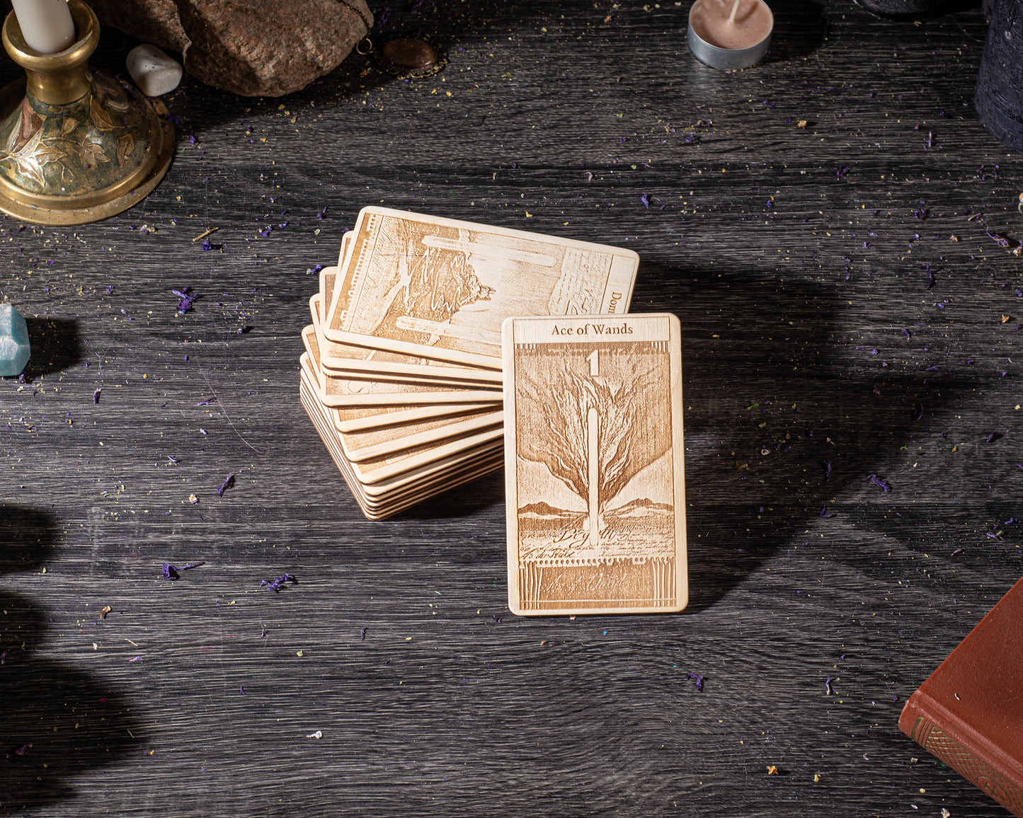 A stack of wooden tarot cards is placed on a wooden surface, with a candle and some other objects in the background.