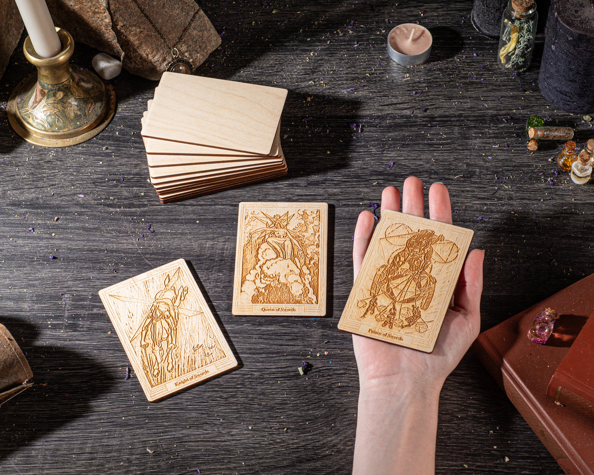 a hand holding three wooden tarot cards on a dark wooden surface, surrounded by various objects such as candles, books, and crystals.