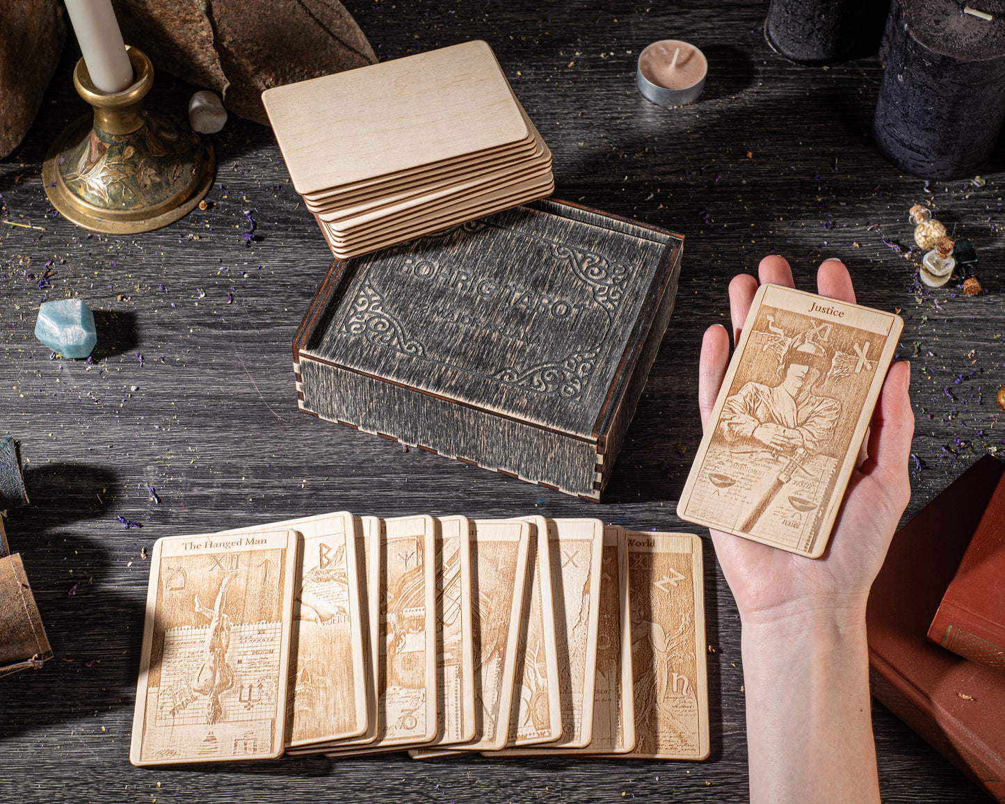 a hand holding a wooden tarot card, surrounded by a collection of wooden cards and a wooden box on a dark wooden surface.