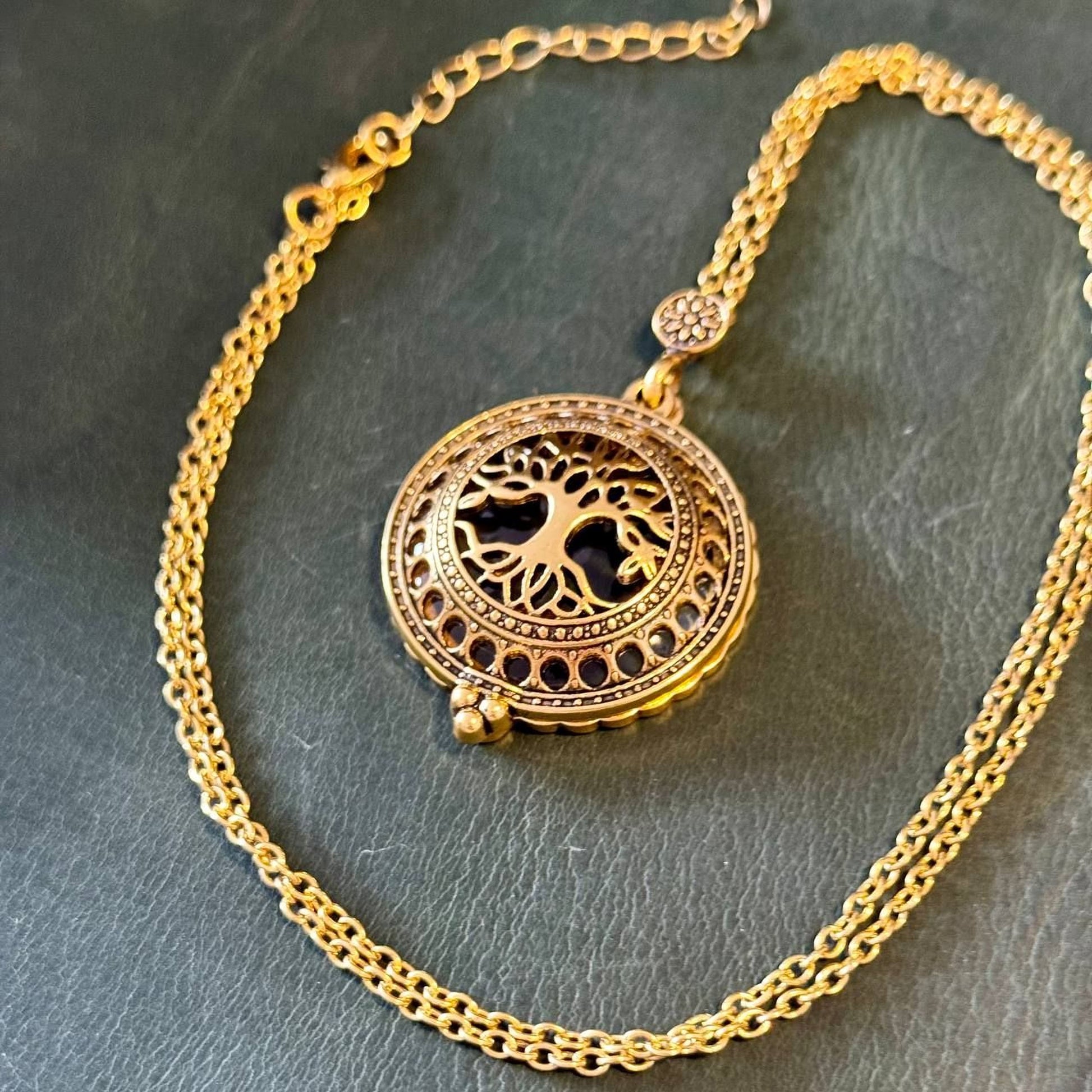 A gold-colored pendant necklace with a circular pendant featuring a tree design.