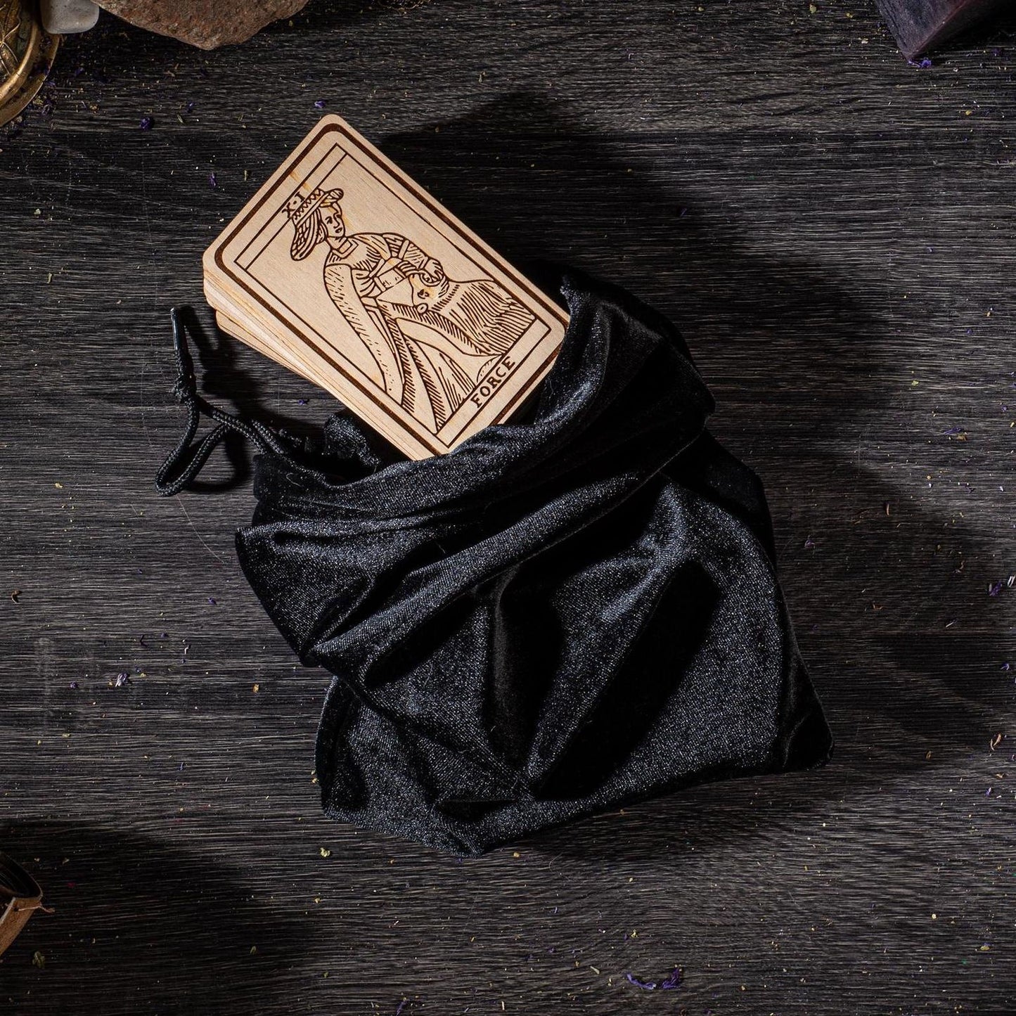 A wooden tarot card is placed inside a black velvet pouch on a wooden surface.