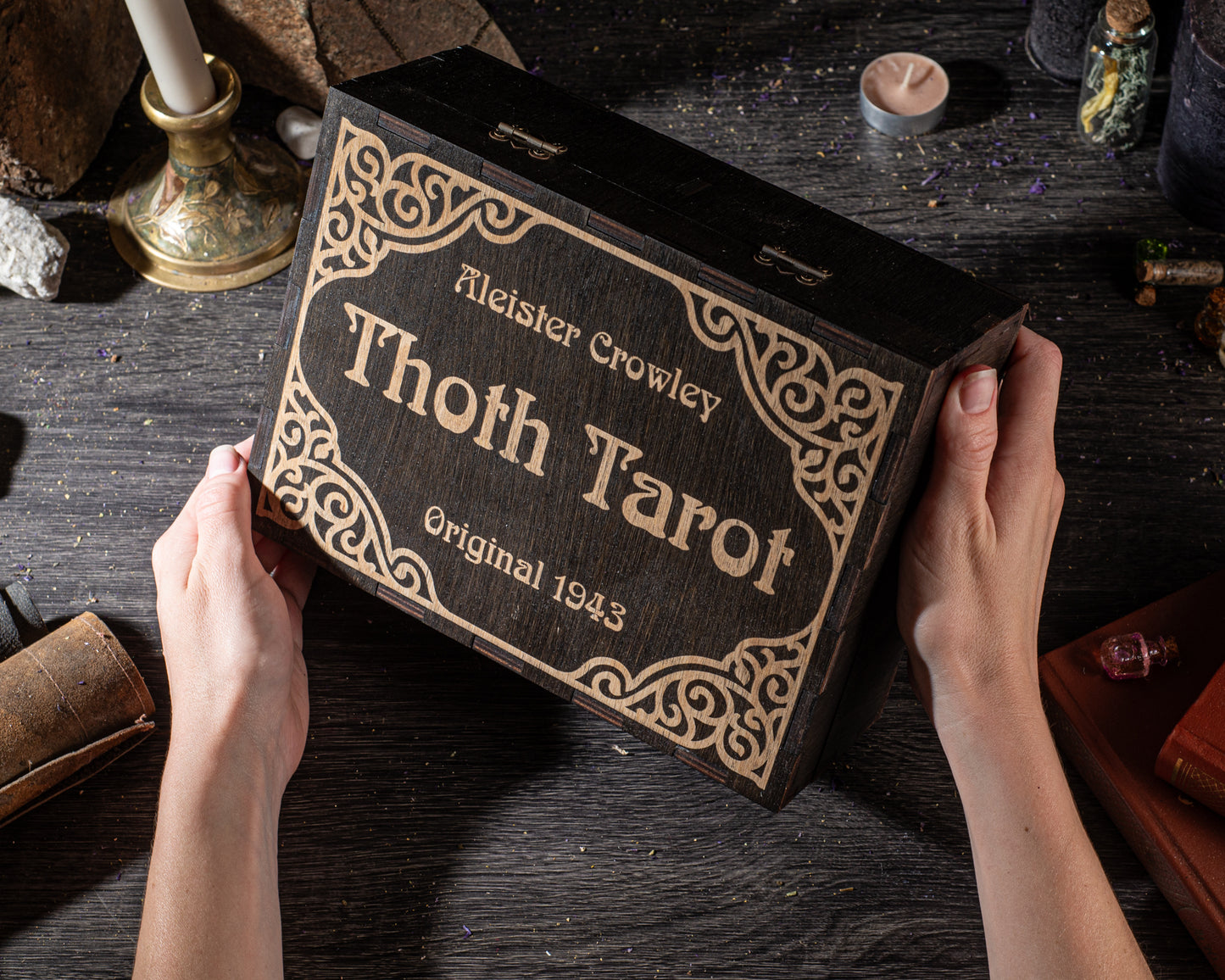 A person's hands holding a wooden box with a decorative border, which appears to be a tarot card box.