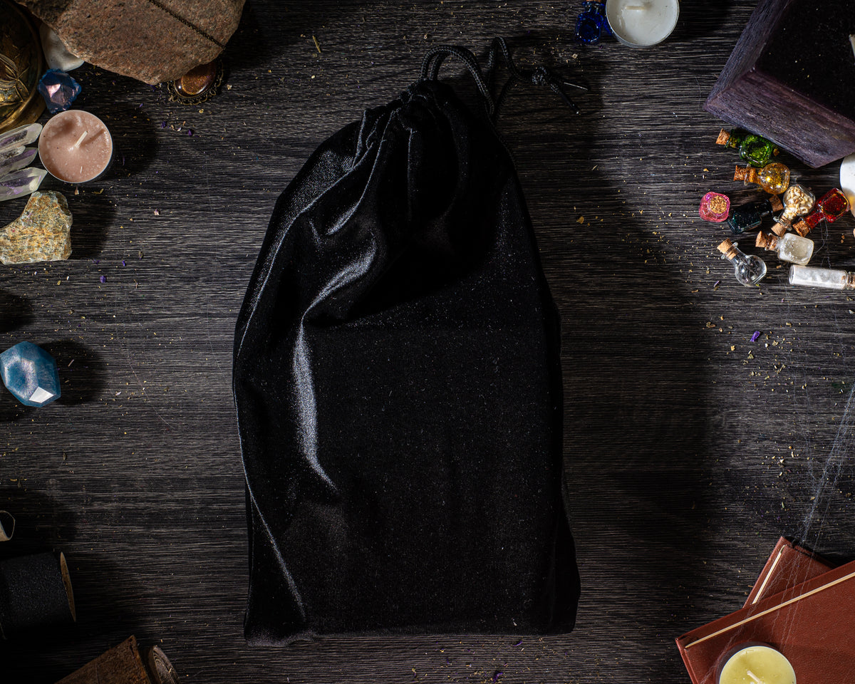 A black velvet pouch is placed on a wooden surface, surrounded by various objects such as gemstones, candles, and books.