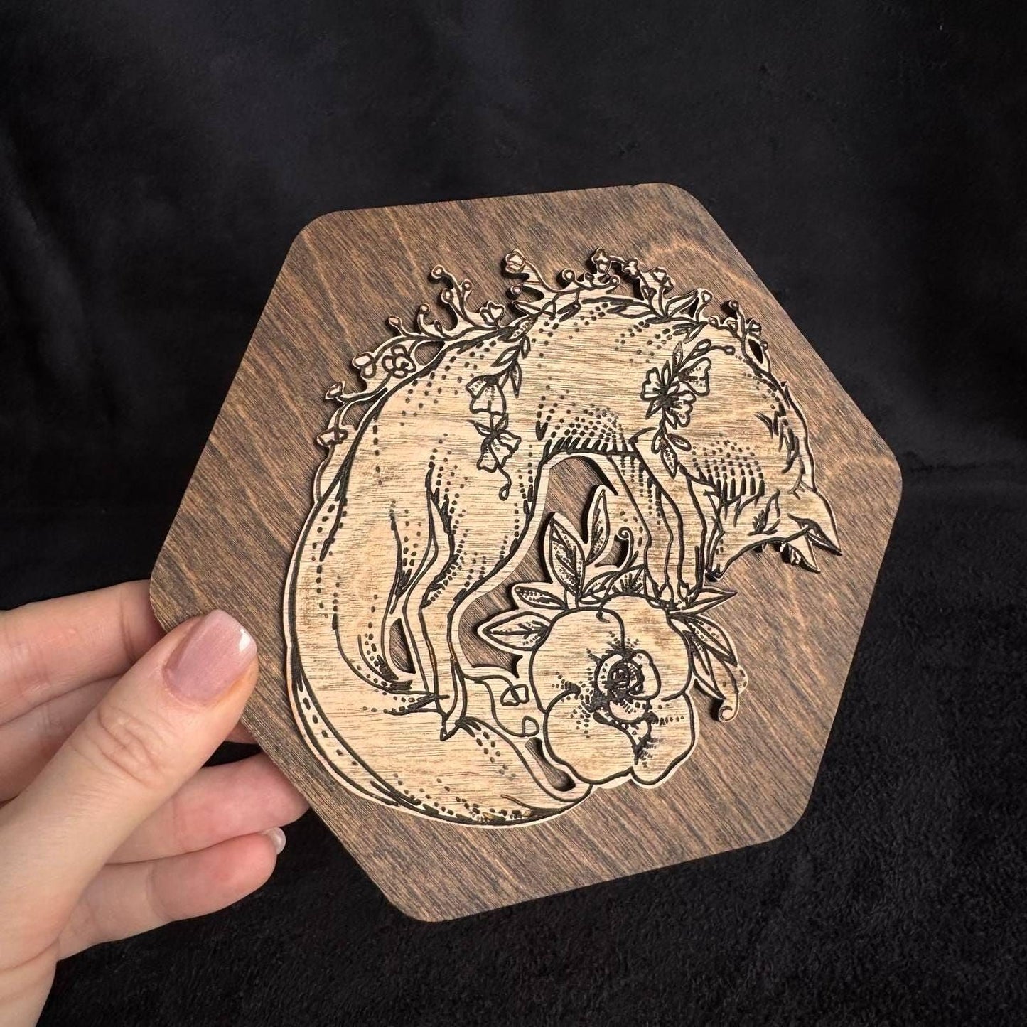 A hand is holding a wooden object with a carved design of a fox surrounded by flowers.