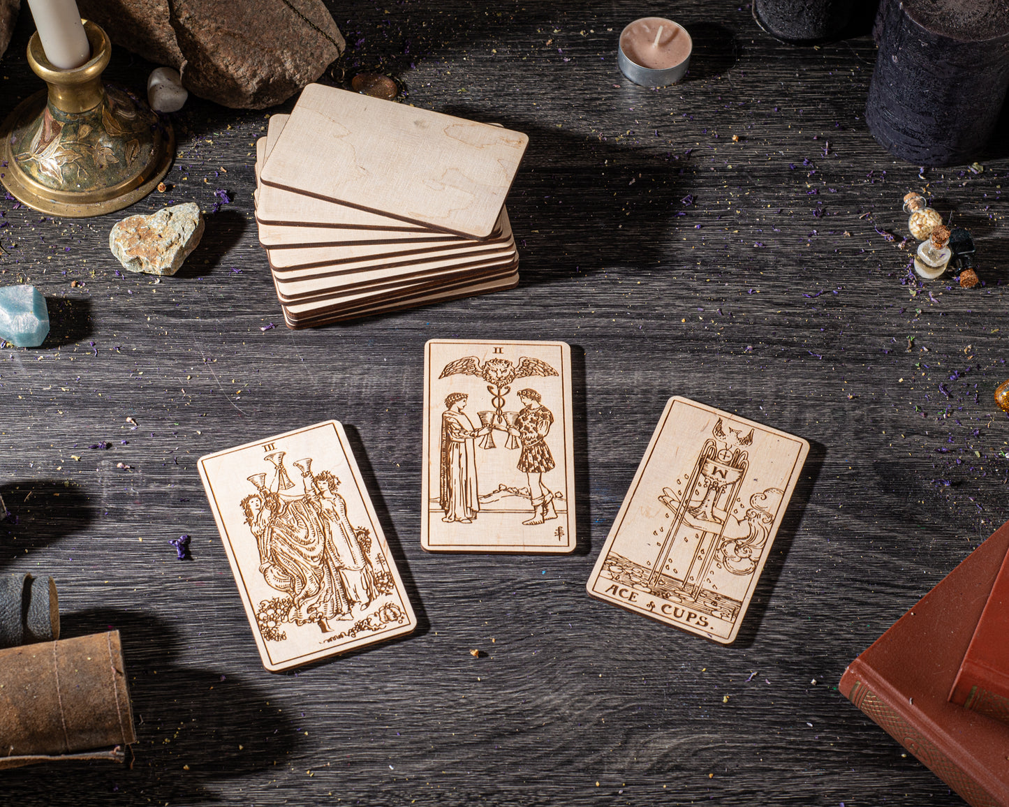 three wooden tarot cards with intricate designs, arranged on a dark wooden surface alongside various objects such as candles, crystals, and books.