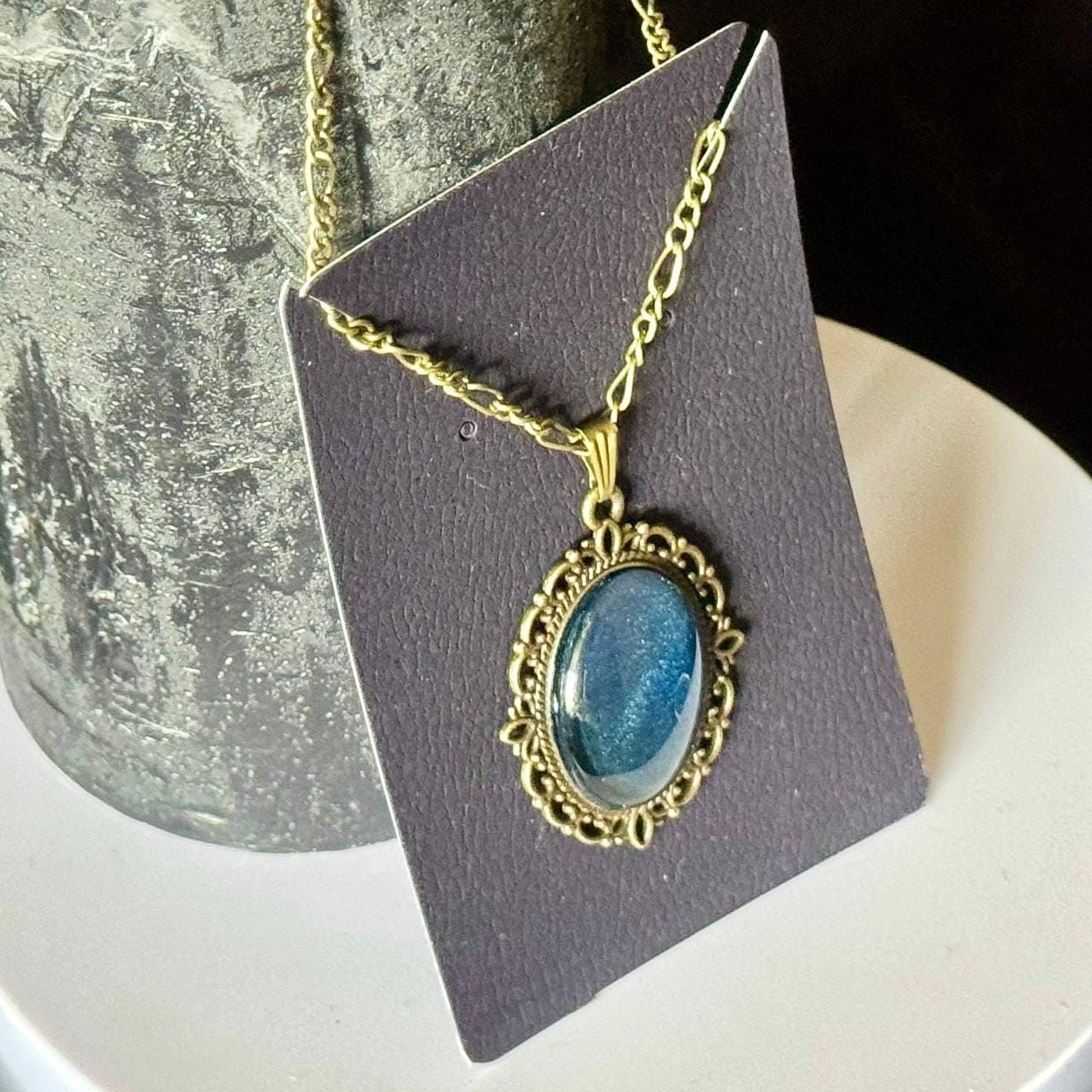 A necklace with a blue stone pendant is displayed on a dark gray card.