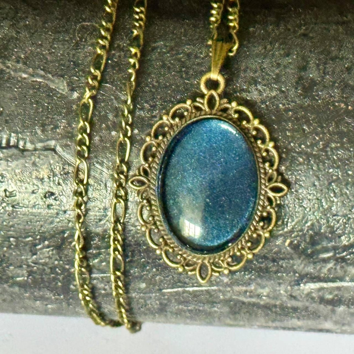 A gold-colored necklace with a blue gemstone pendant is displayed on a metal surface.
