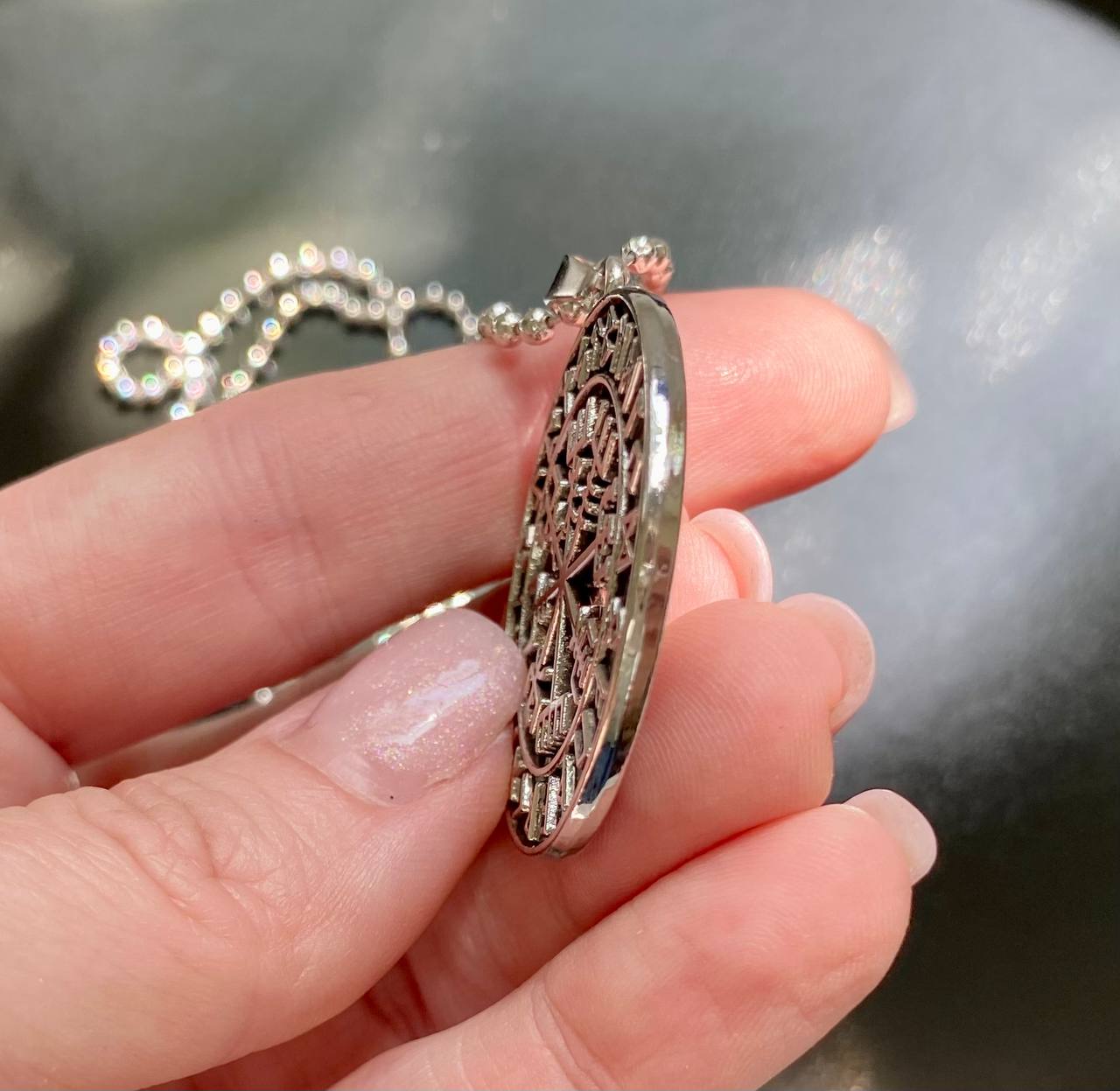 A hand holding a silver pendant with an intricate design.