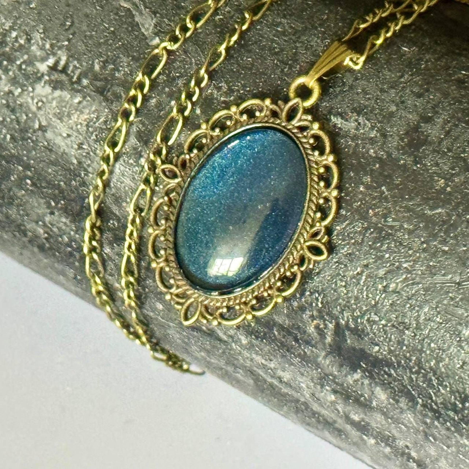 A close-up image of a pendant with a blue gemstone, hanging from a gold chain.