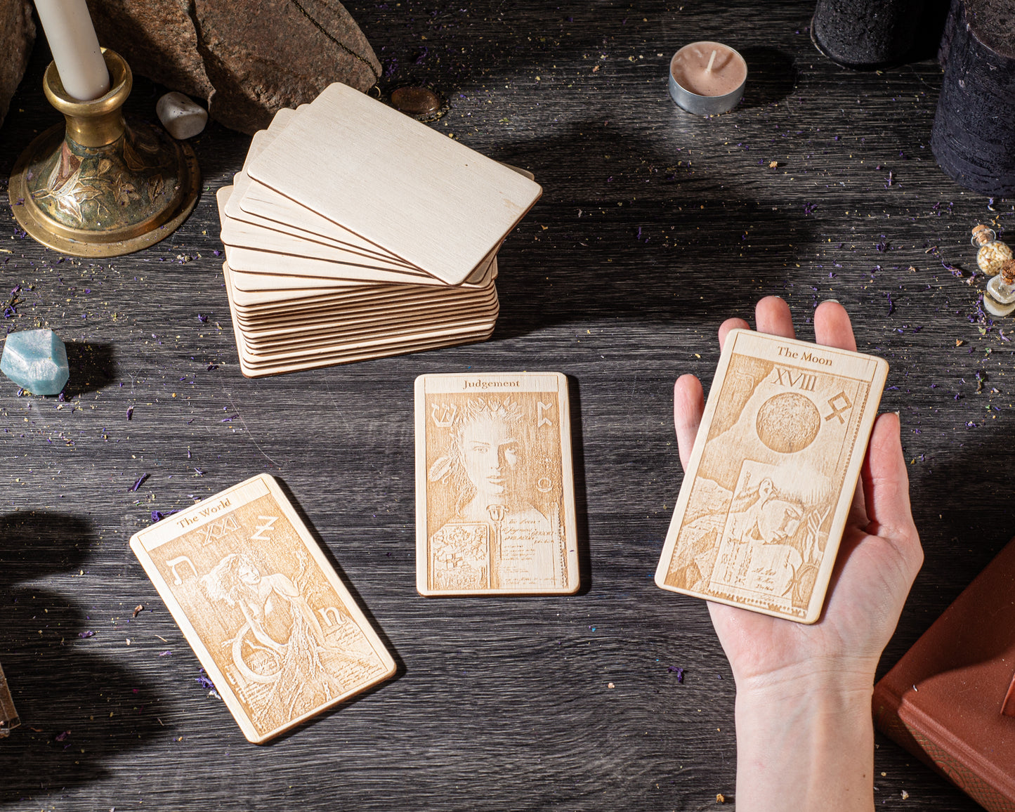 a hand holding three wooden tarot cards, with a stack of additional cards visible in the background.