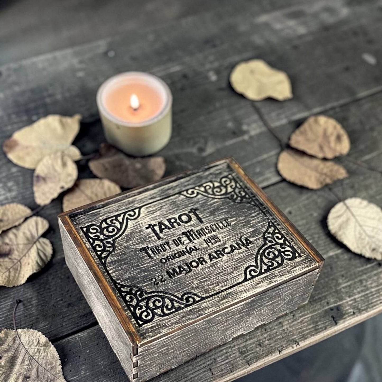 A wooden box with a candle and some dried leaves on a wooden surface.