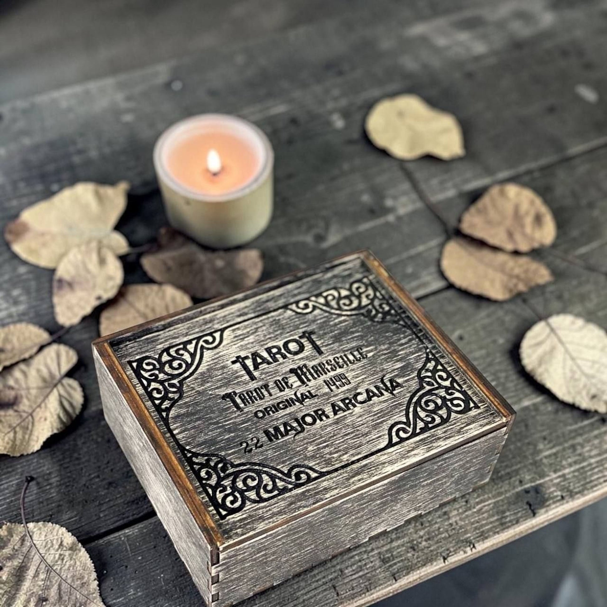 A wooden box with a candle and some dried leaves on a wooden surface.