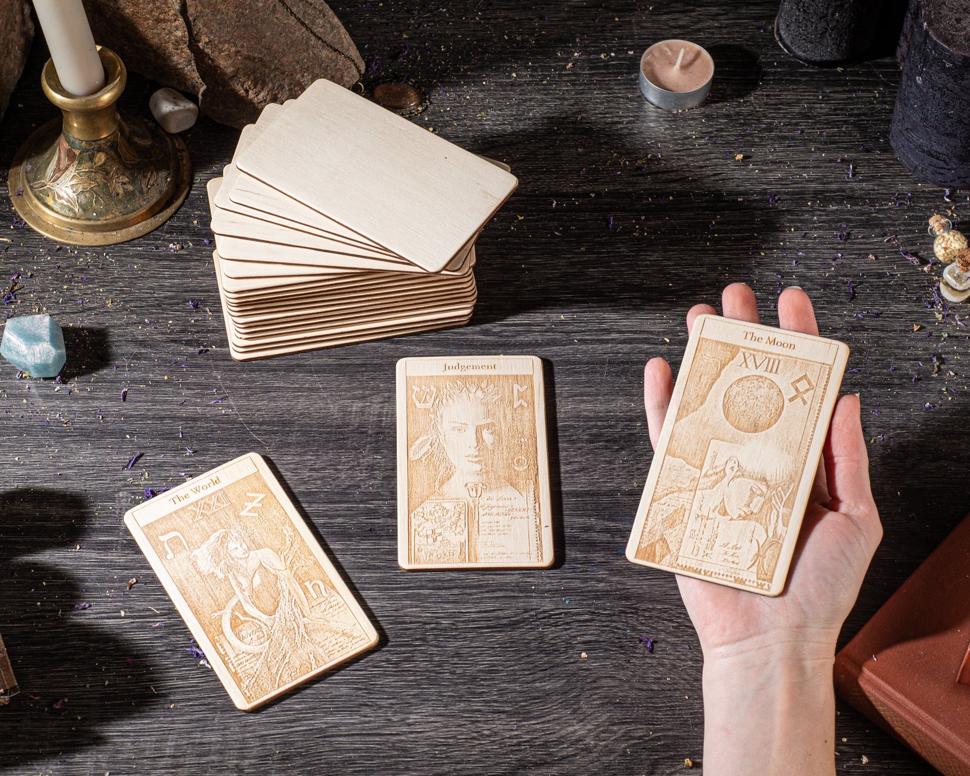 a hand holding three wooden tarot cards, with a stack of additional cards visible in the background.
