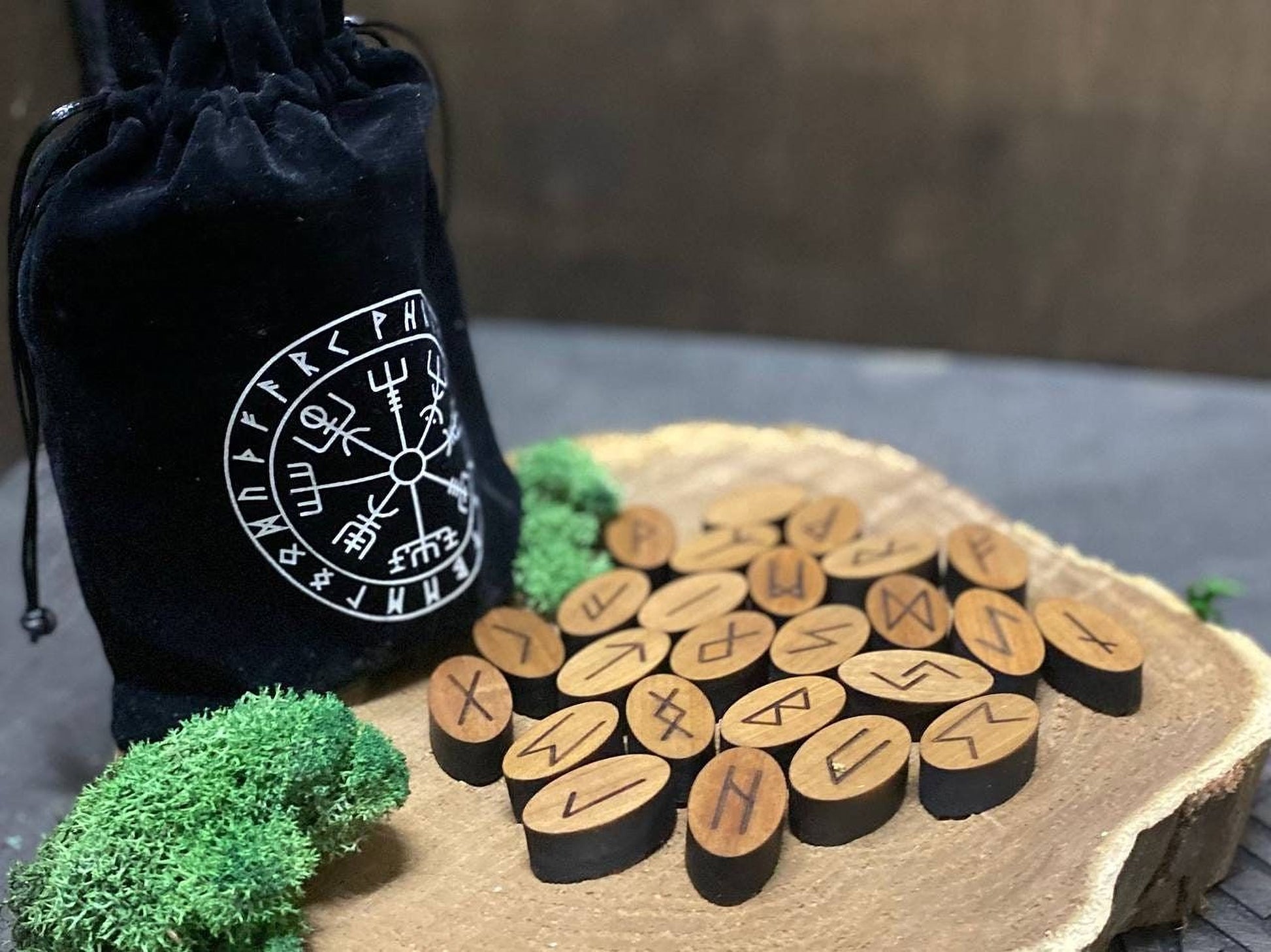 a collection of wooden Viking symbols arranged on a wooden surface, with a black bag featuring a white Viking symbol in the background.