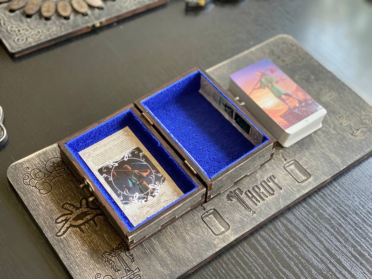 a wooden box with a blue interior, containing a tarot card and a deck of playing cards, placed on a wooden surface.