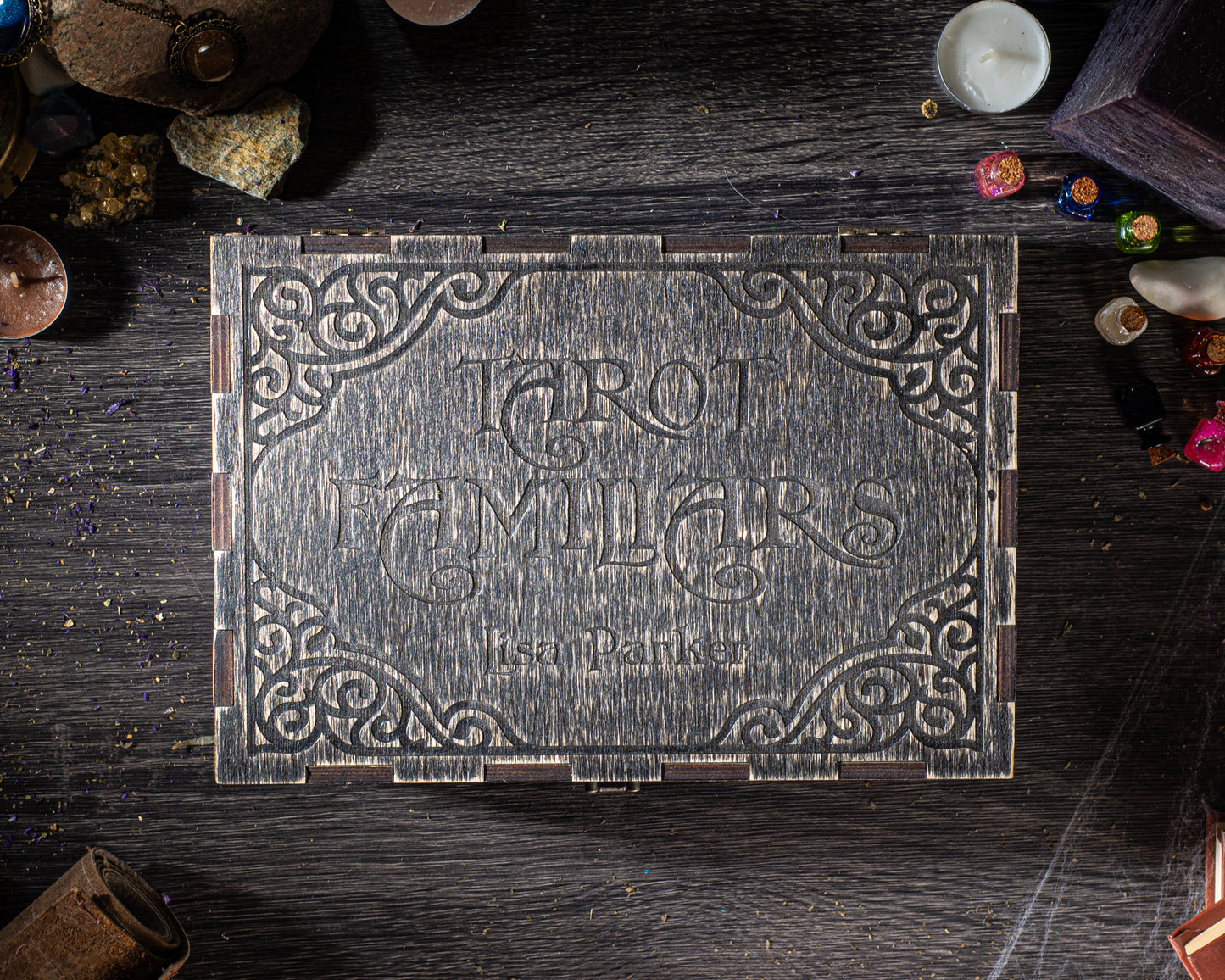 a wooden box with a decorative design, surrounded by various objects such as candles, crystals, and other items on a wooden surface.