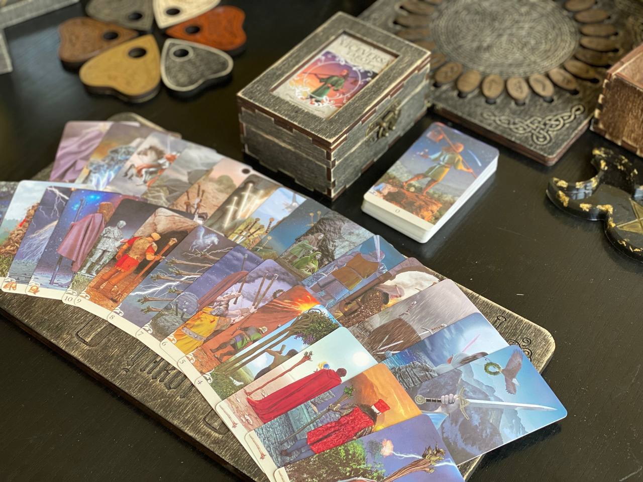 a collection of tarot cards and a wooden box on a table, with various other items such as a heart-shaped object and a metal box in the background.