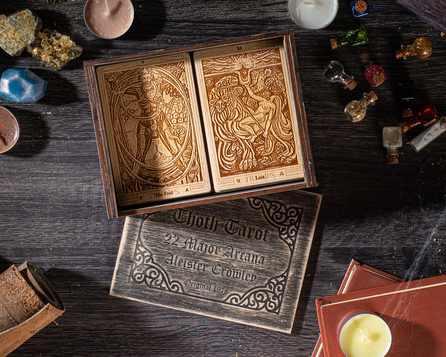 a wooden box with two tarot cards inside, along with various other items such as candles, books, and crystals on a wooden surface.
