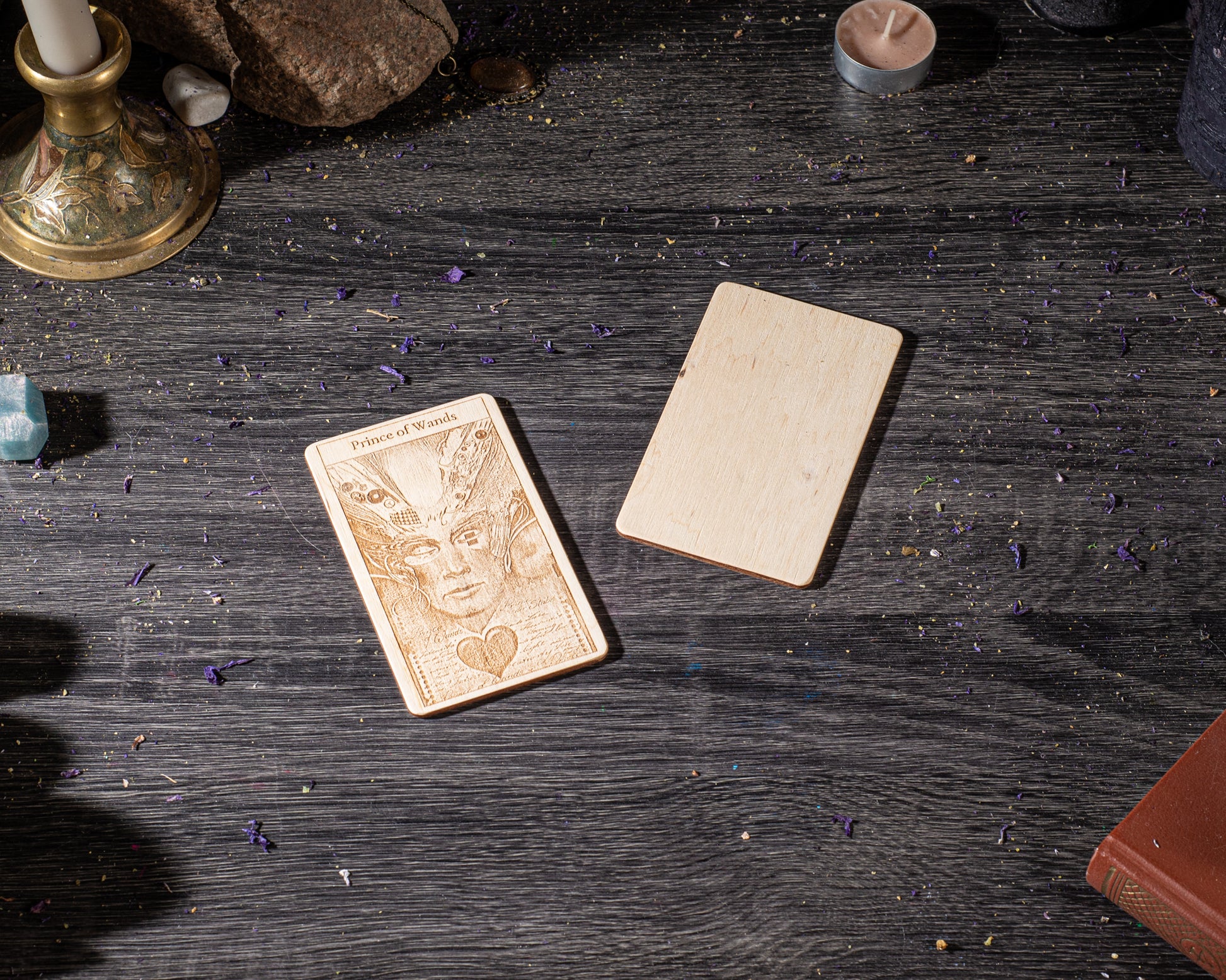 a wooden card with an intricate design, placed on a dark wooden surface alongside a candle and some other objects.