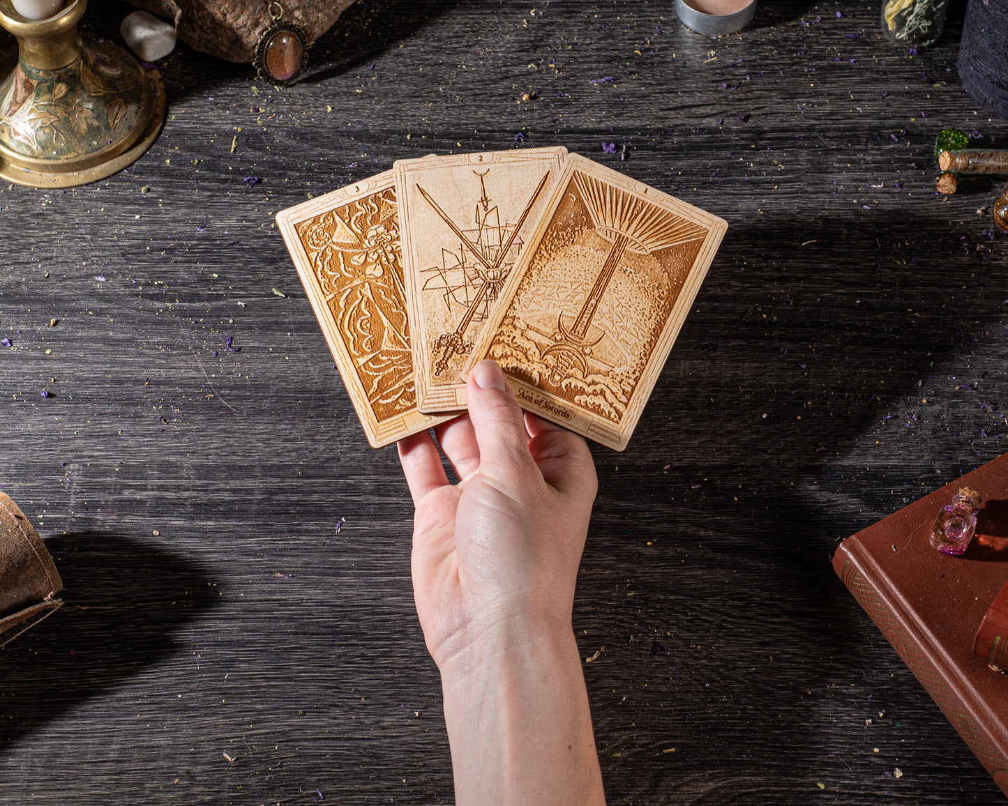 A hand holding three wooden tarot cards against a dark wooden background.