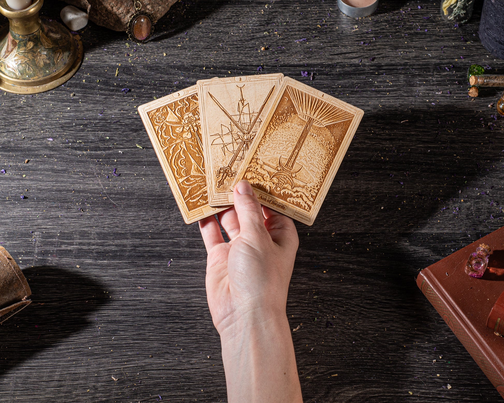 A hand holding three wooden tarot cards against a dark wooden background.