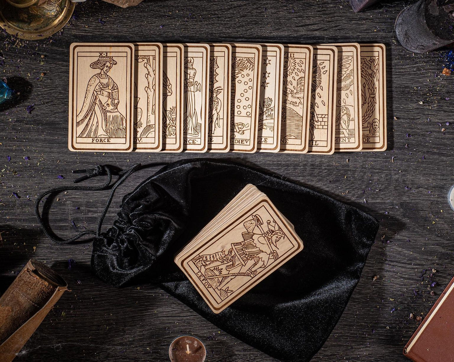 a collection of wooden tarot cards arranged on a wooden surface, along with a black velvet pouch and a small wooden object.