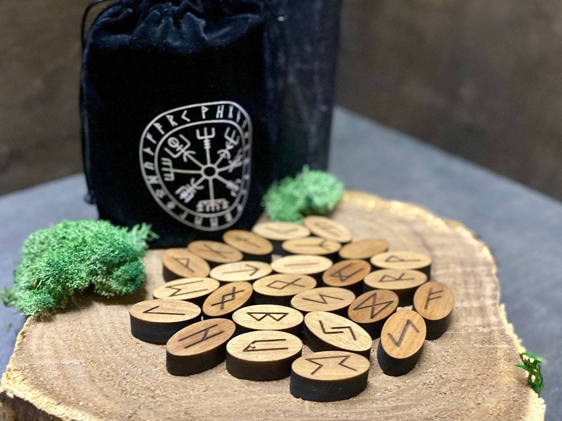 a collection of wooden symbols arranged on a wooden surface, with a black bag featuring a white design in the background.