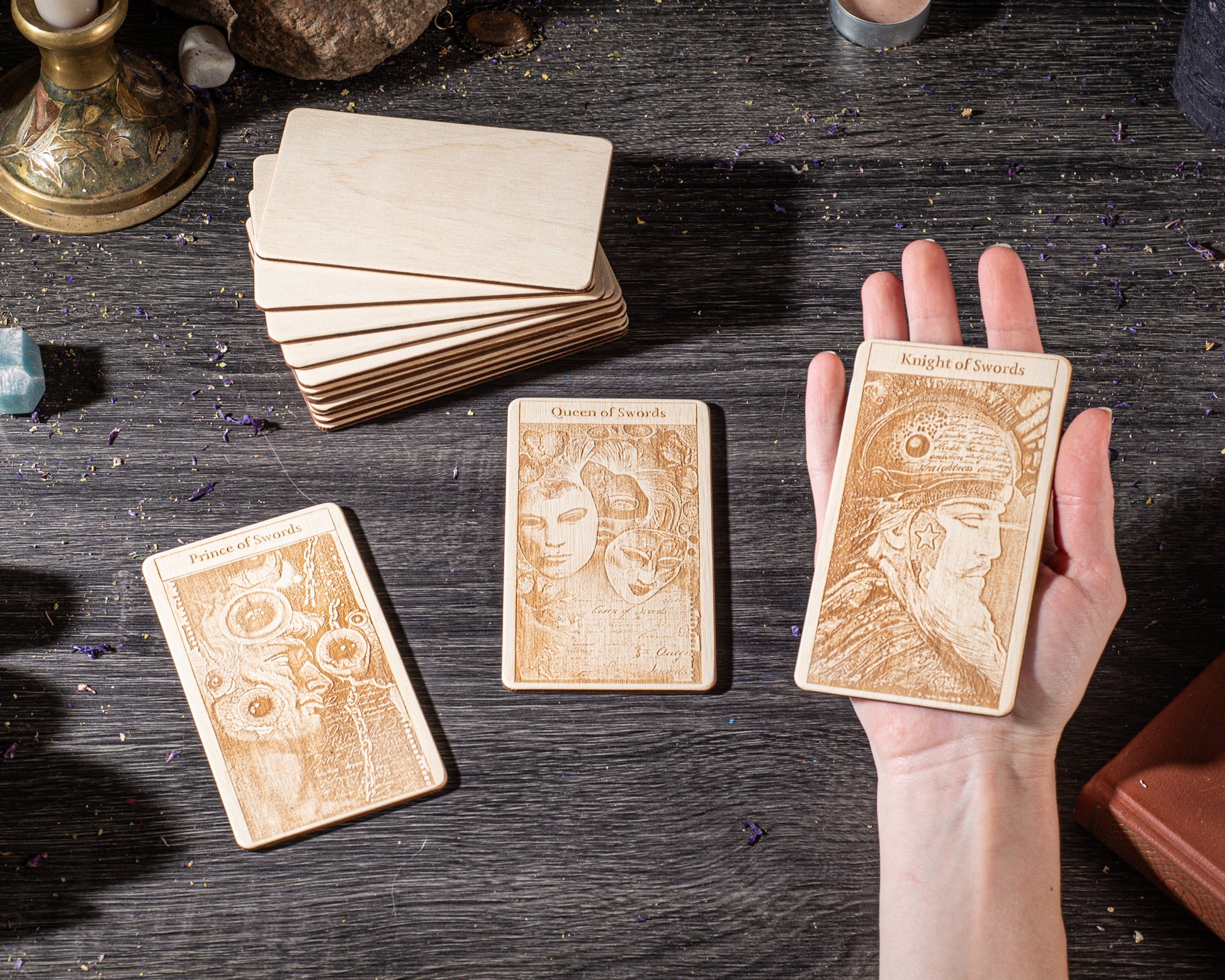 a hand holding three wooden tarot cards, each with a unique design and text, on a dark wooden surface.