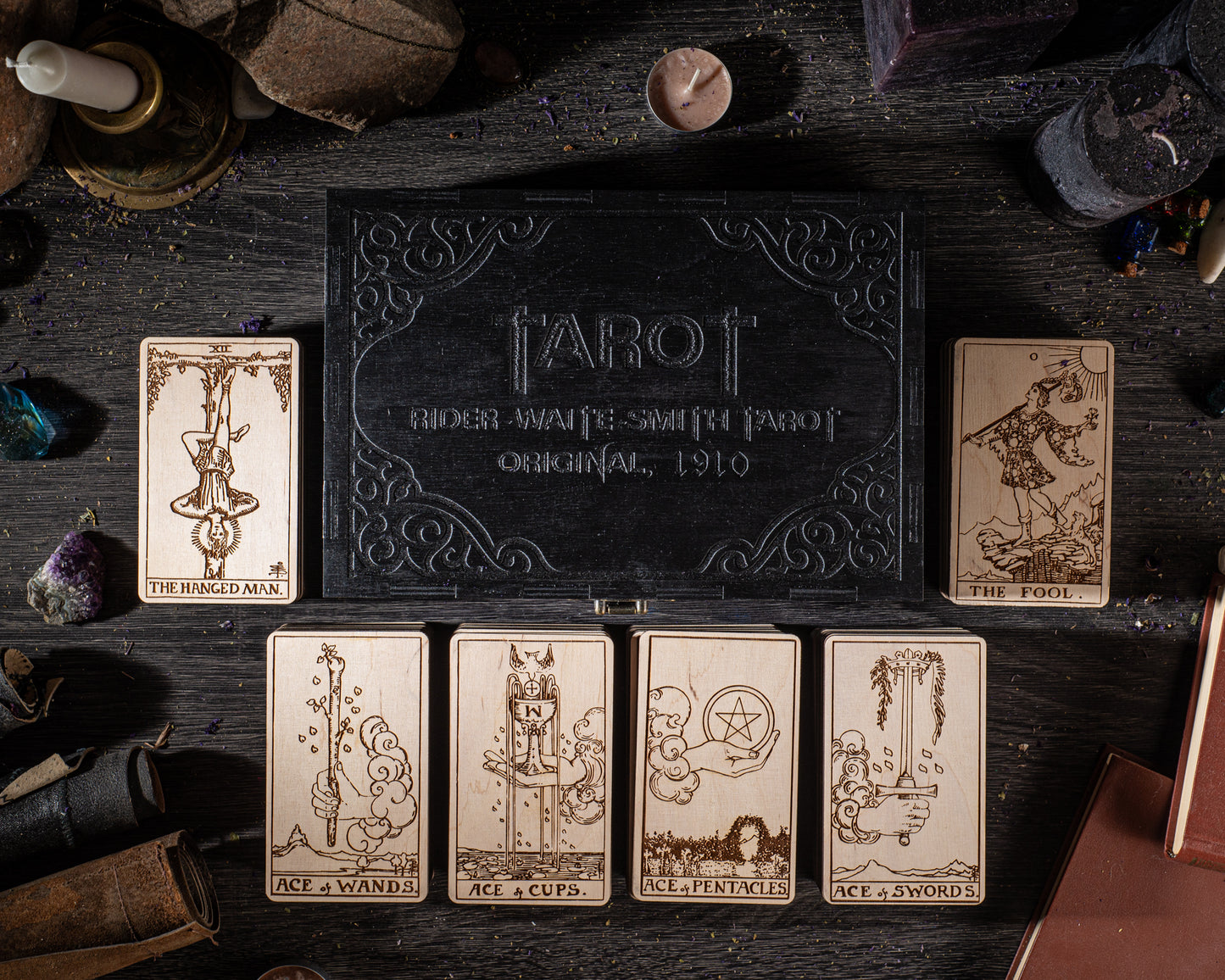 a tarot deck with six cards displayed on a wooden surface, along with various objects such as a candle, crystals, and books.