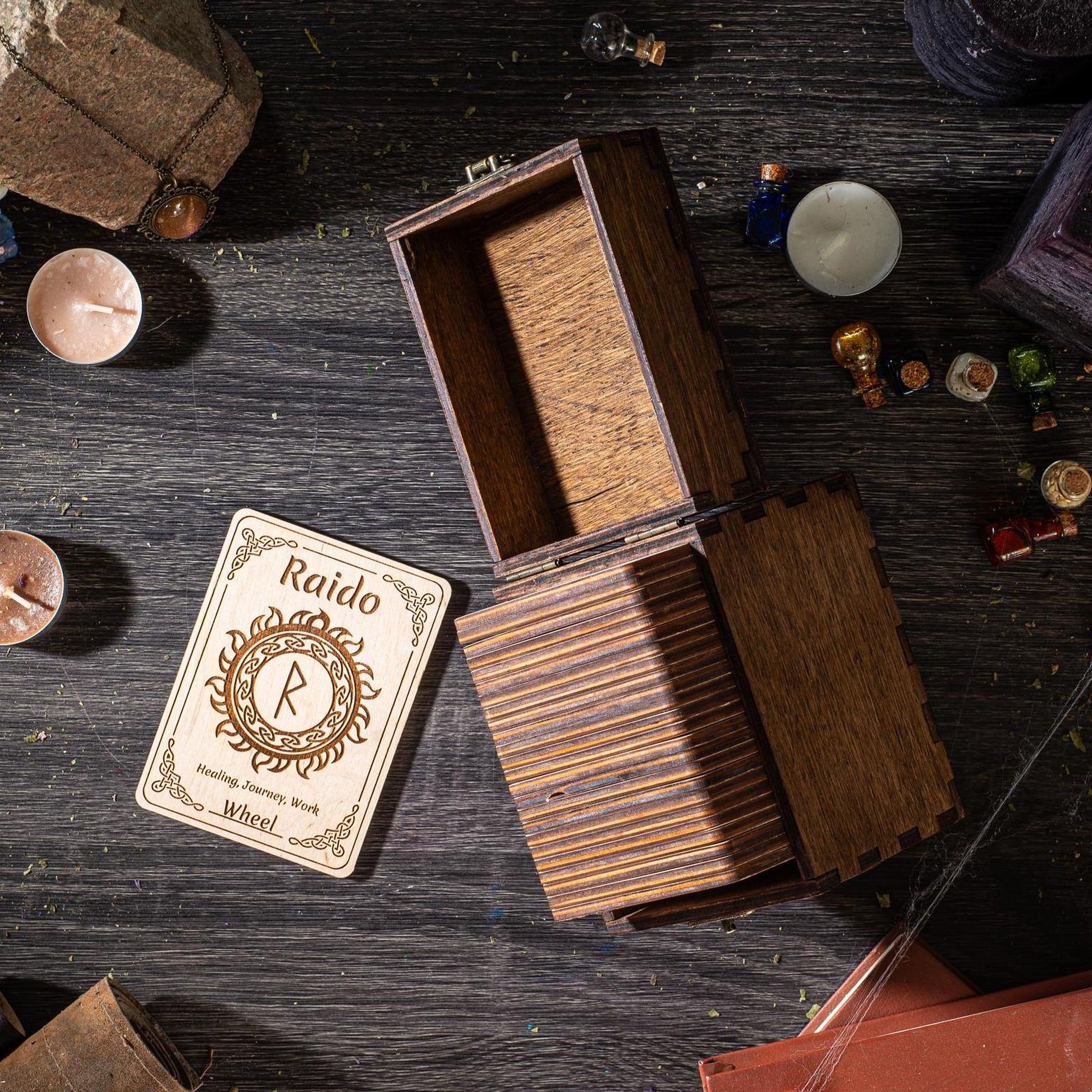 a wooden box with a card inside, along with various objects such as candles, a small figurine, and other miscellaneous items scattered on a dark wooden surface.