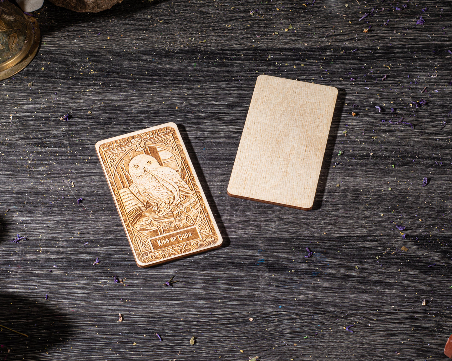 a wooden card with an owl design, placed on a wooden surface with scattered purple flowers.