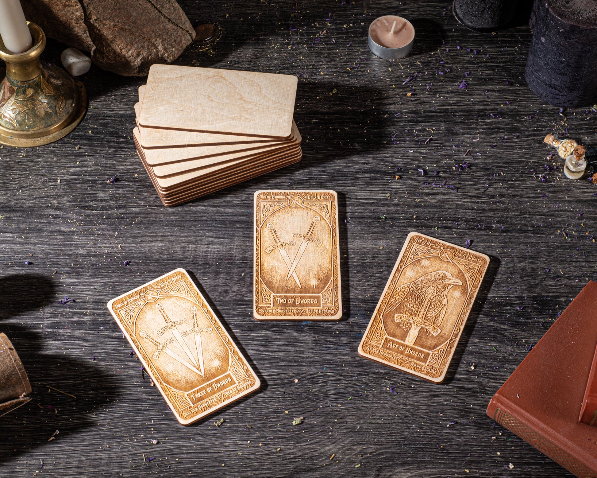 three wooden cards with intricate designs, placed on a dark wooden surface alongside various objects such as candles, books, and other items.