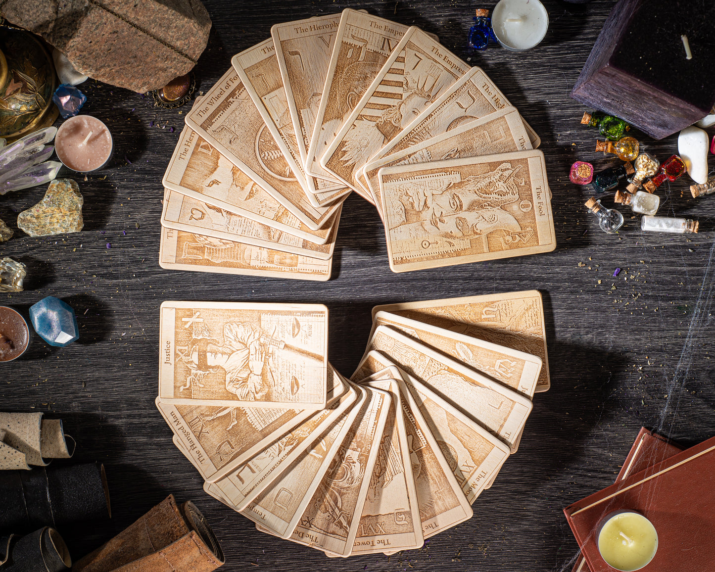 A collection of wooden tarot cards arranged in a fan-like pattern on a dark wooden surface, surrounded by various objects such as crystals, candles, and books.