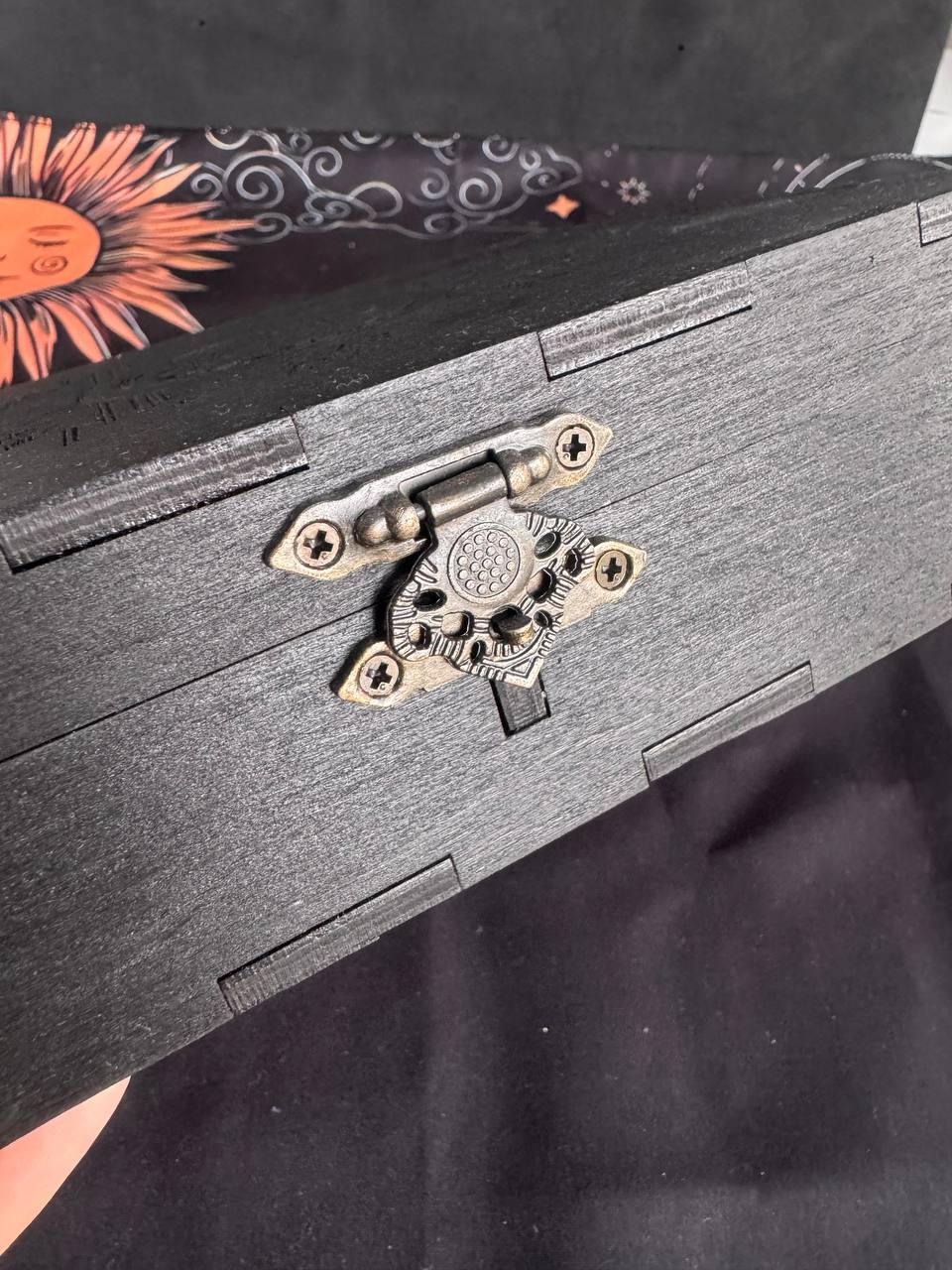a close-up view of a black wooden box with a decorative metal clasp on the front.