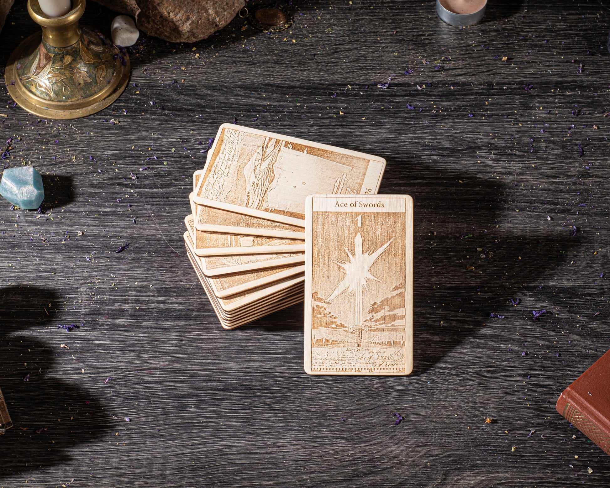 A stack of wooden cards with intricate designs, including a card with a star and the text "Ace of Swords" on it, is placed on a dark wooden surface.