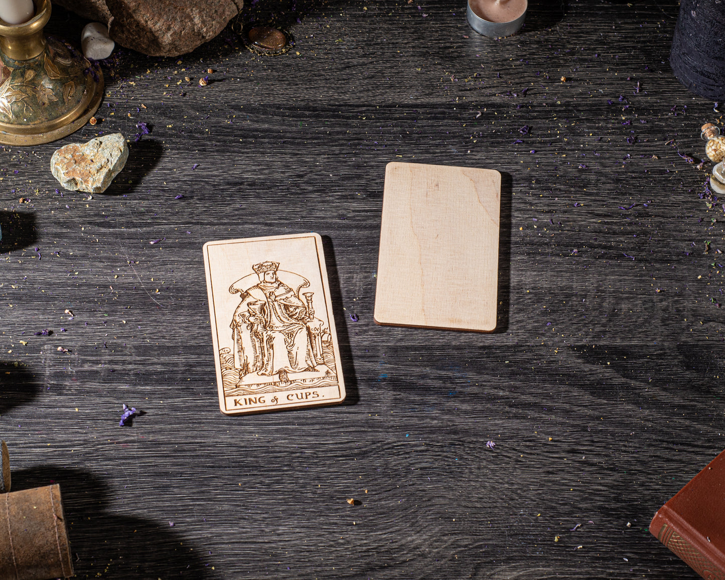 a wooden card with a tarot card design, placed on a wooden surface with various objects around it, including a candle, a book, and some crystals.