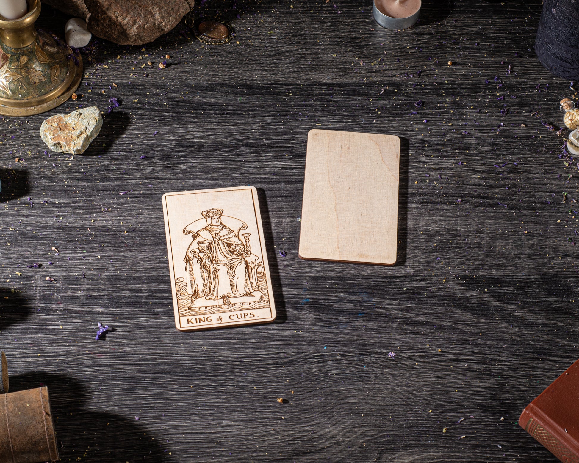 a wooden card with a tarot card design, placed on a wooden surface with various objects around it, including a candle, a book, and some crystals.