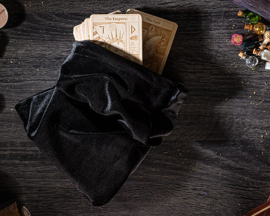 A black velvet pouch containing several tarot cards is placed on a dark wooden surface, with scattered objects around it.