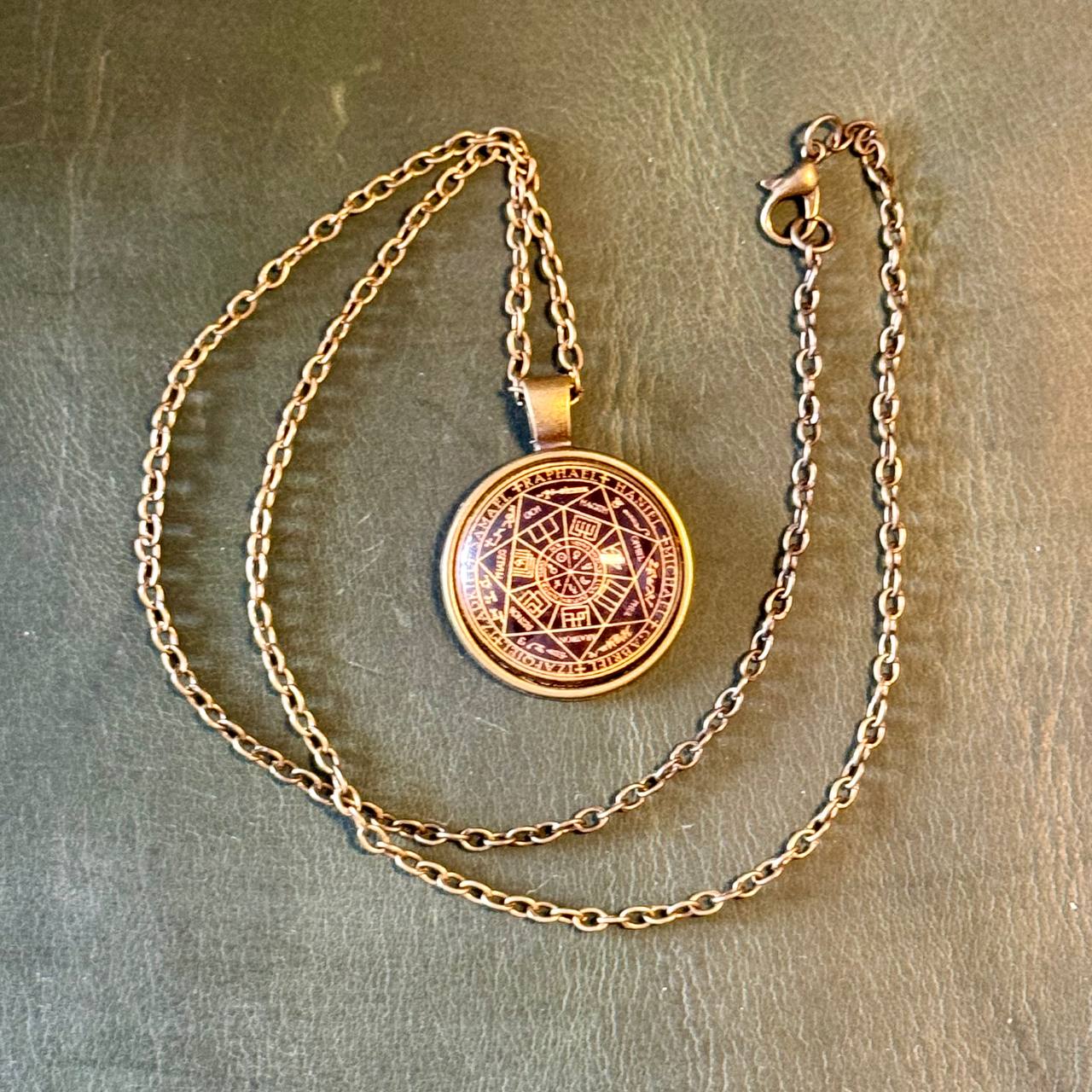 A gold-colored pendant necklace with a circular medallion featuring a geometric design.