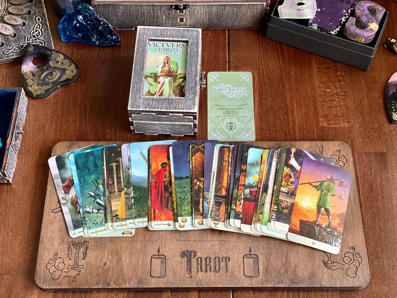a collection of tarot cards arranged on a wooden board, along with a deck of playing cards and a crystal.