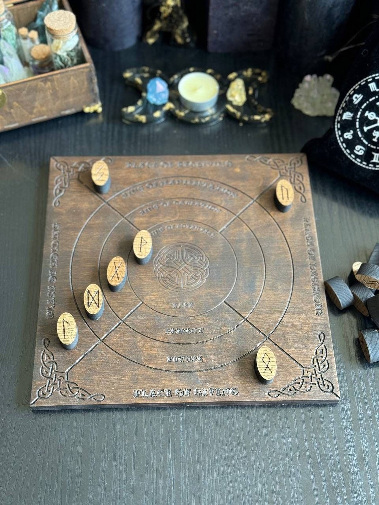 a wooden board with various symbols and text, including the word "KRAK OF GIVING". The board appears to be a game board or a decorative piece, with a few small wooden pieces placed on top of it.