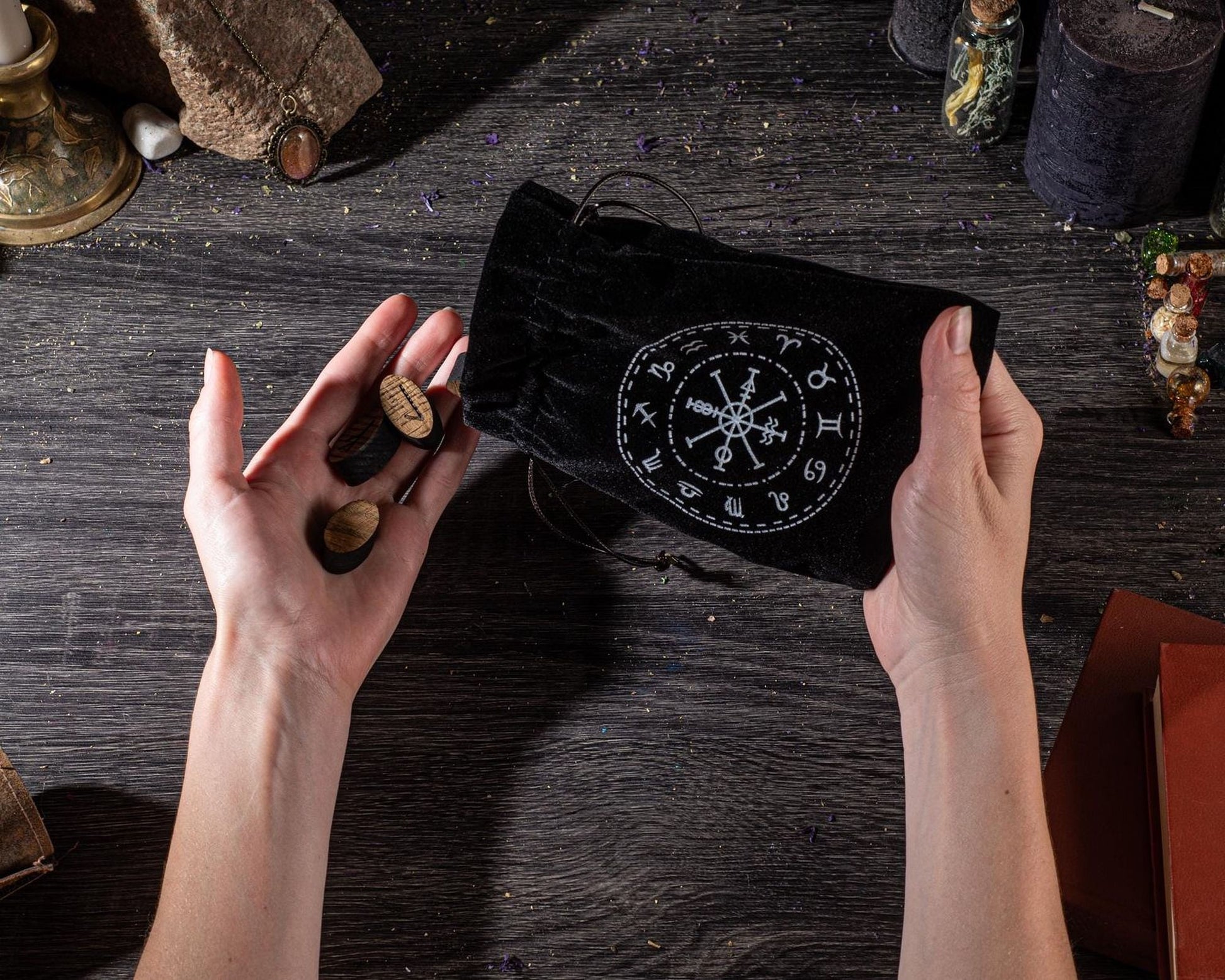 A person's hands holding a black pouch with a compass design, surrounded by various objects on a wooden surface.