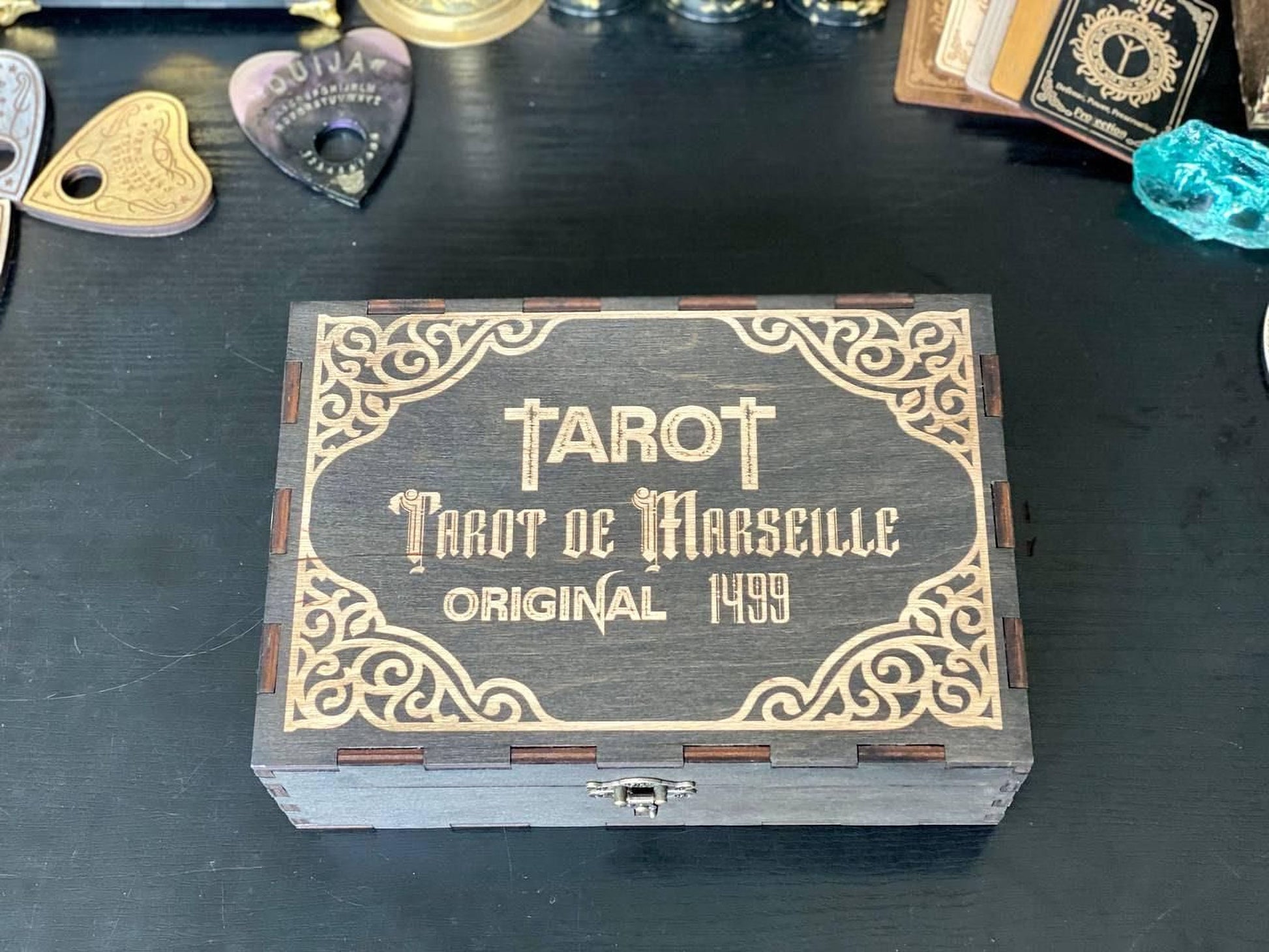 A wooden box with decorative borders and text, placed on a dark surface.
